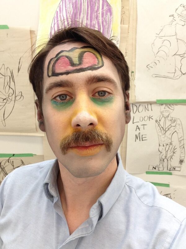 A portrait of a light-skinned male presenting person with a drawing on his forehead, green concealer under his eyes, and yellow blush on his cheeks