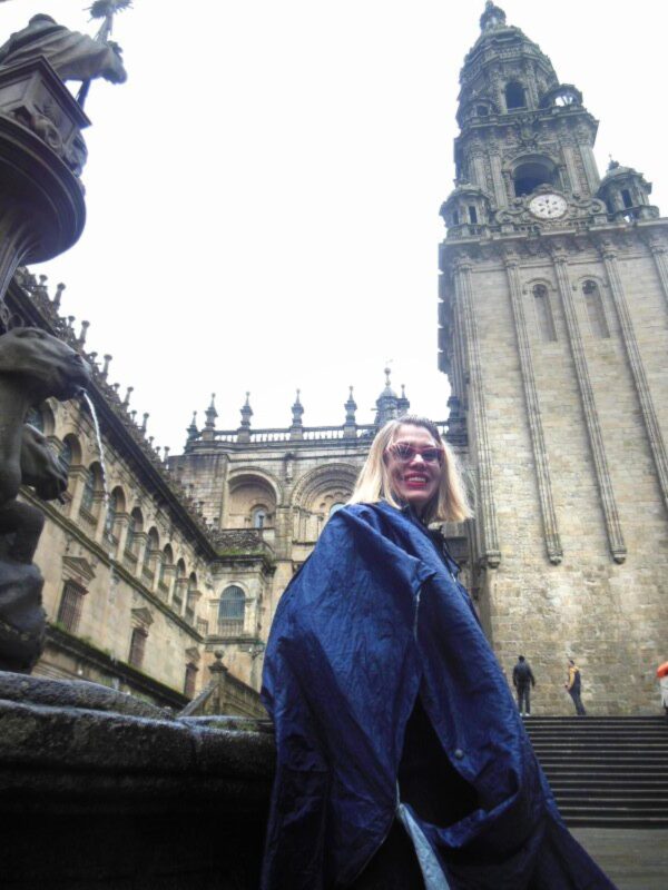 A woman poses at the foot of a large bell tower on a cloudy day