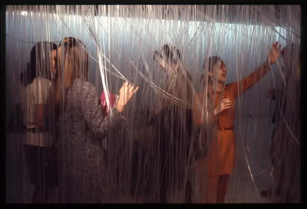People explore a room filled with clear plastic strings hanging from the ceiling