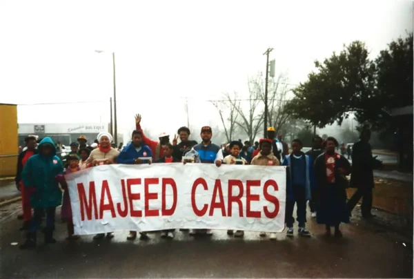 A group of people holding a white parade banner with red text reading Majeed Cares