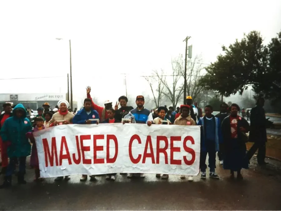 A group of people holding a white parade banner with red text reading Majeed Cares