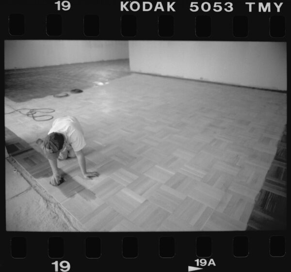 A person on hands and knees installs wooden parquet flooring