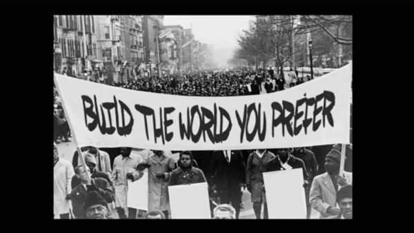 Black and white photo of a crowd of people holding a banner stating Build the world you prefer