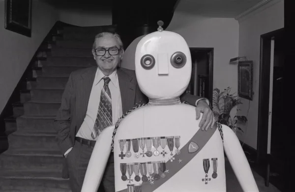 Black and white photo of a man standing on a staircase next to a sculpture resembling a robot general