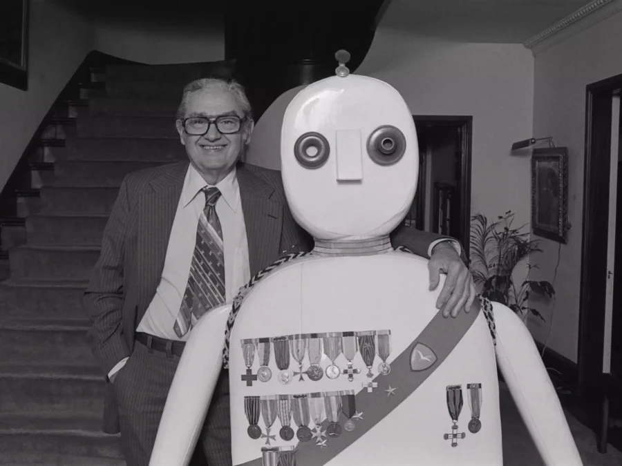 Black and white photo of a man standing on a staircase next to a sculpture resembling a robot general