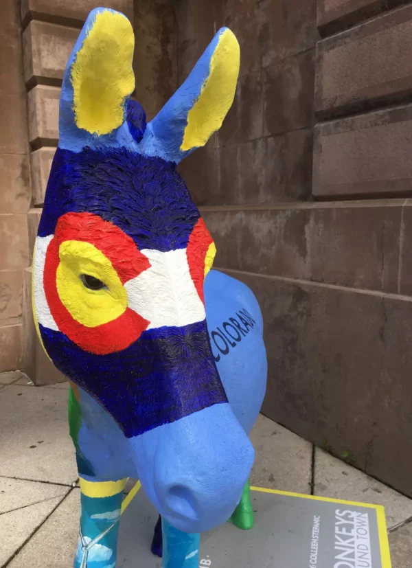 A blue donkey statue with its face painted in the style of the Colorado flag