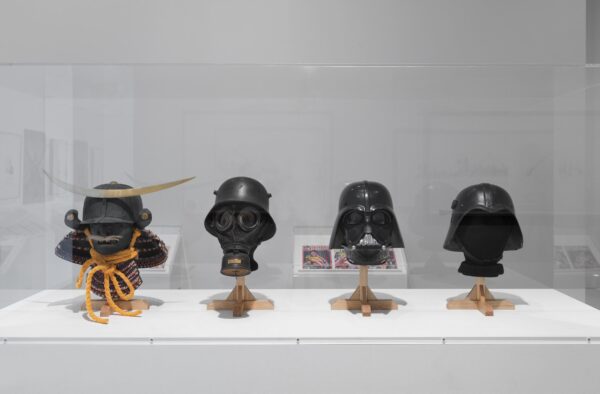 Four military helmets and masks in a glass vitrine