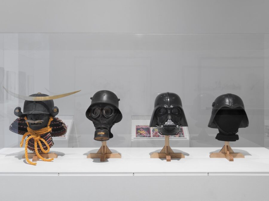 Four military helmets and masks in a glass vitrine