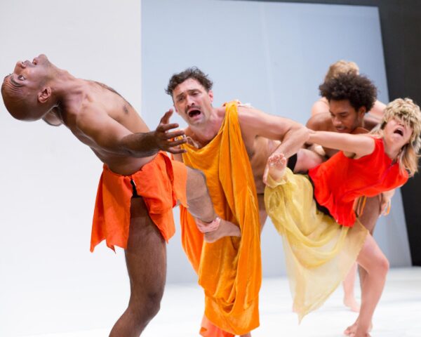 Four actors on a stage dressed in various sized orange colored sheets in a type of tug of war with each other