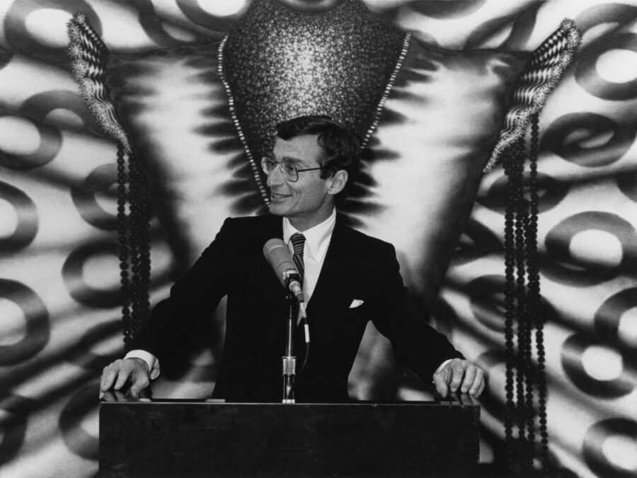 black and white photo of a man standing at a podium with a large artwork behind him