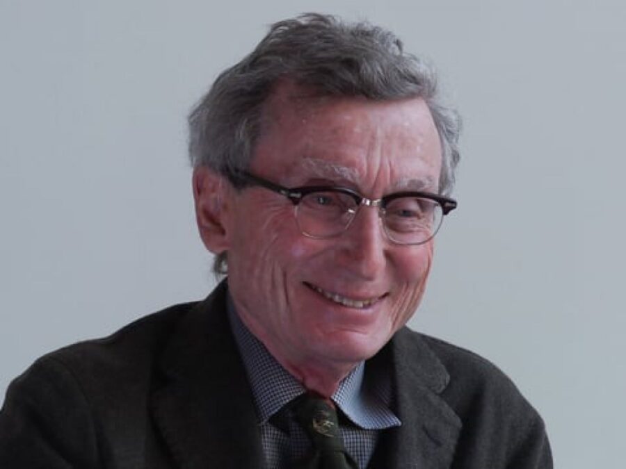 An older man in glasses smiling against a gray backdrop