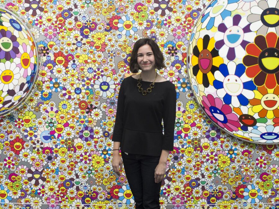 A person poses between two flower orbs in front of a wall covered in happy daisy faces