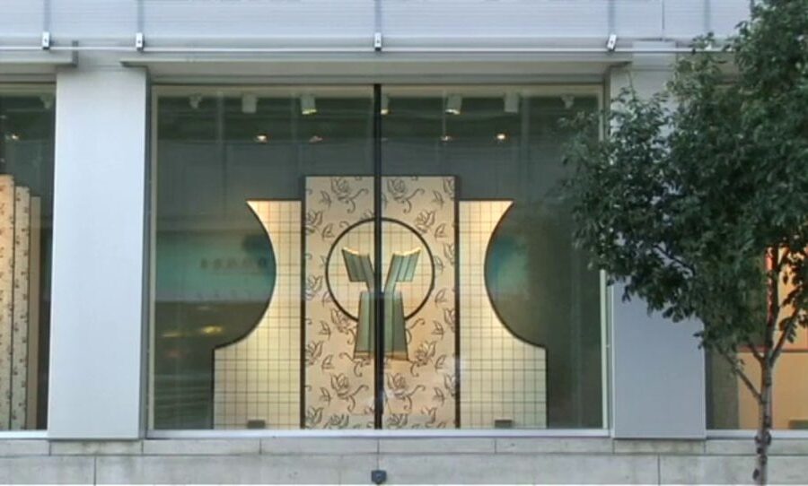 A window display viewed from outside featuring a dress against a floral and cream art deco backdrop