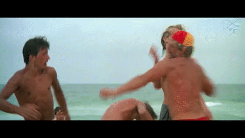 Four topless males get into a fist fight in front of a large body of water.