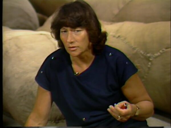 Grainy color image of a woman in front of large mounds of yellowed material
