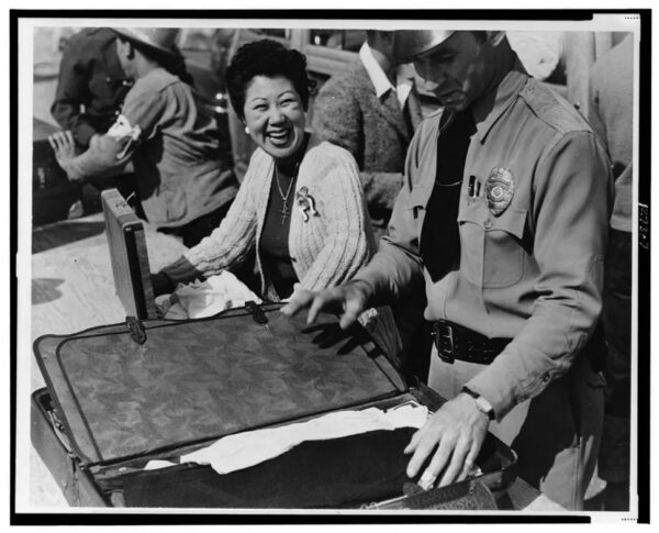 A woman smiles as a uniformed person opens a suitcase