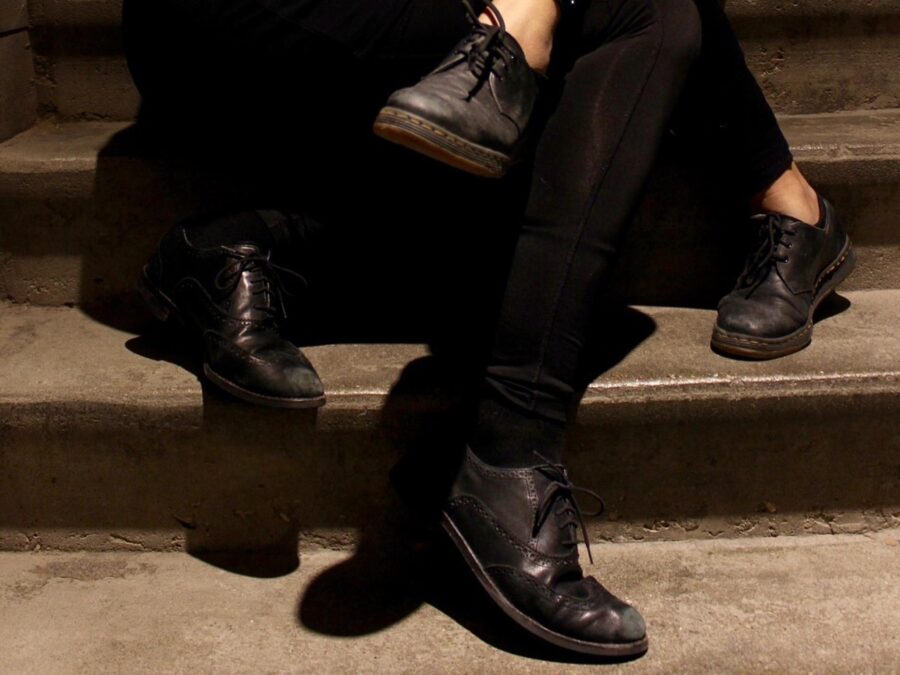 Close up of two sets of legs wearing black pants and black loafers entangled on a set of stairs