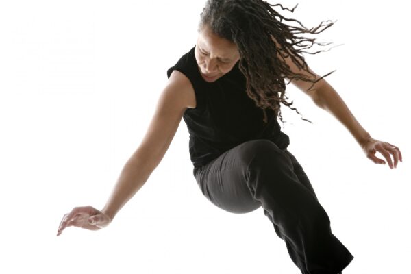 A person with brown hair and medium-dark skin bends at the waist in midair against a white background