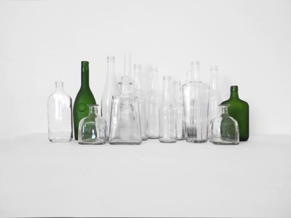 A display of bottles with no labels on them against a grey backdrop. Most are clear bottles, but two at either end are green.