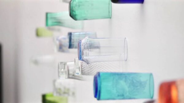 Glasses of all shapes and sizes in greens, blues, clear, and oranges attached to a white wall
