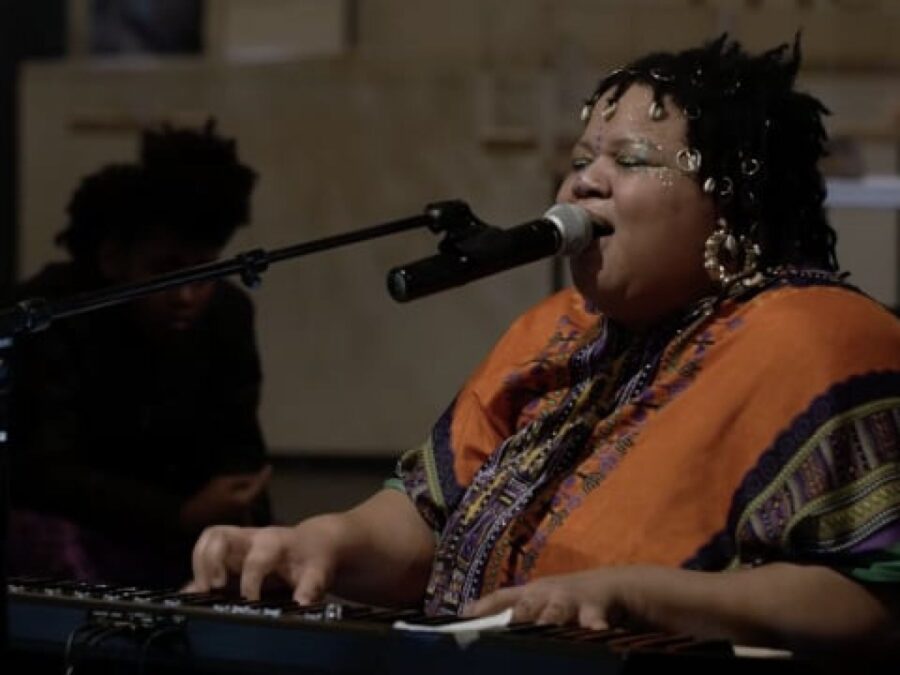 A person sits at a piano while singing into a microphone
