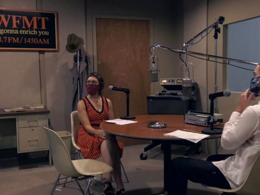 Two people talk in a radio station recording booth