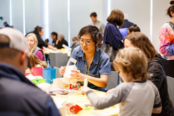 Groups of adults and children sit at tables making crafts