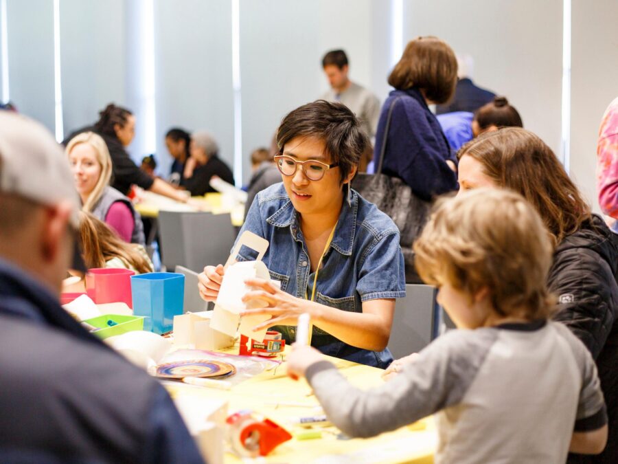 Groups of adults and children sit at tables making crafts