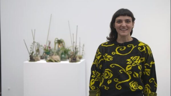 A person in a sweater stands next to a floral arrangement on a white pedestal