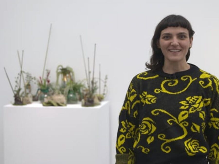 A person in a sweater stands next to a floral arrangement on a white pedestal