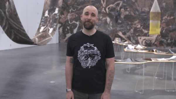 A person in a black t-shirt stands in a gallery with fabric draping from the ceiling and walls