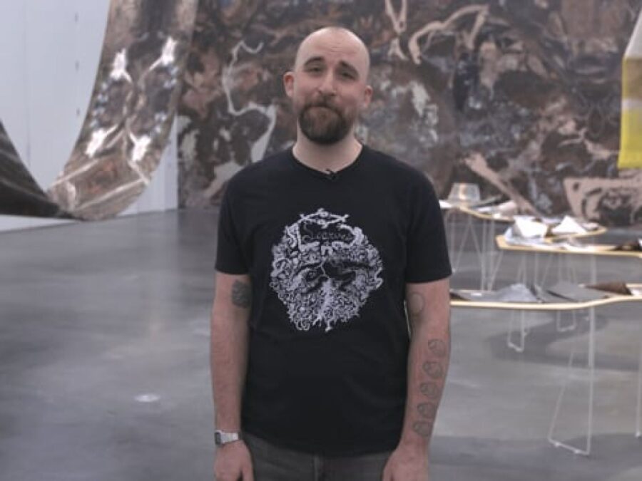 A person in a black t-shirt stands in a gallery with fabric draping from the ceiling and walls