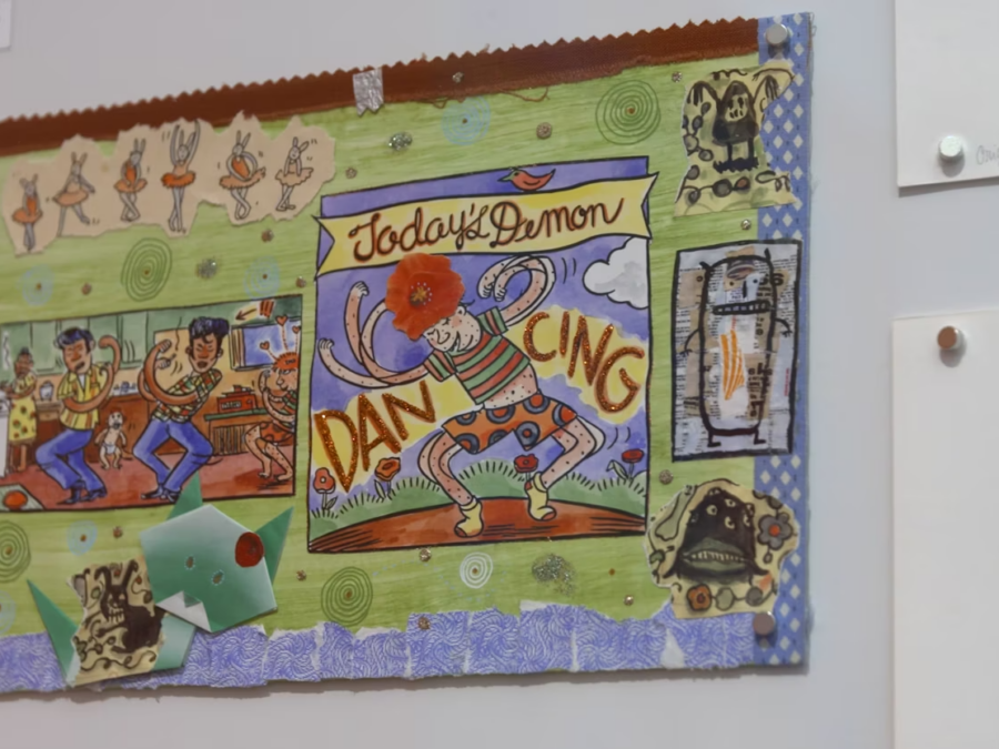 Close up of a drawing hanging on a white wall with other drawings pinned up just of camera