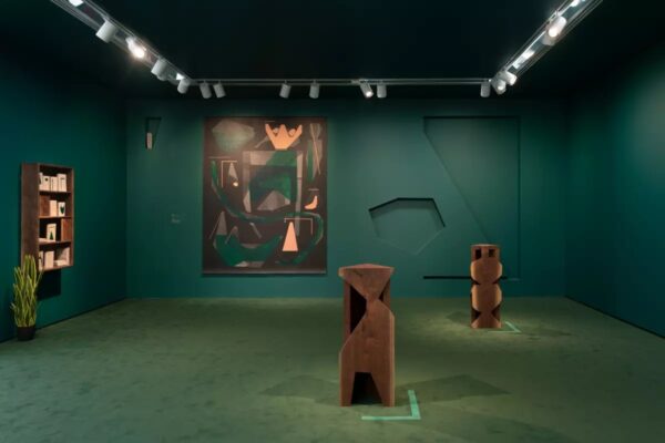 A room featuring teal-green walls and carpet with wooden sculptures on the floor and an abstract painting on the back wall