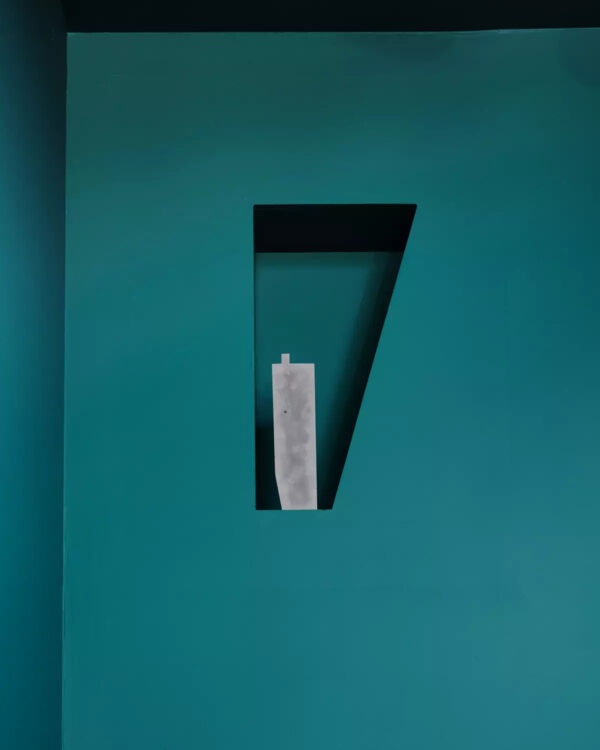 A white object within a narrow, deep-set niche on a dark teal wall.