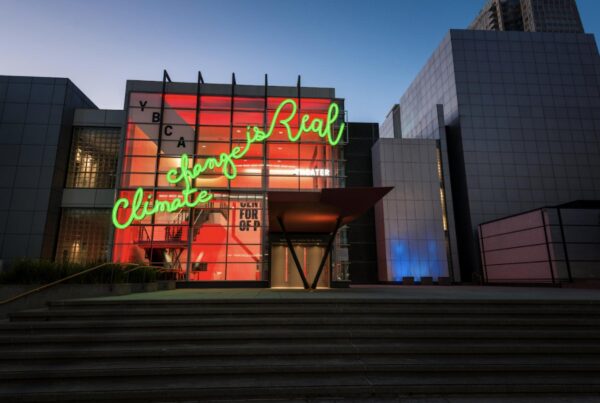 exterior of building with large neon green light formed into cursive text on the windows reading climate change is real