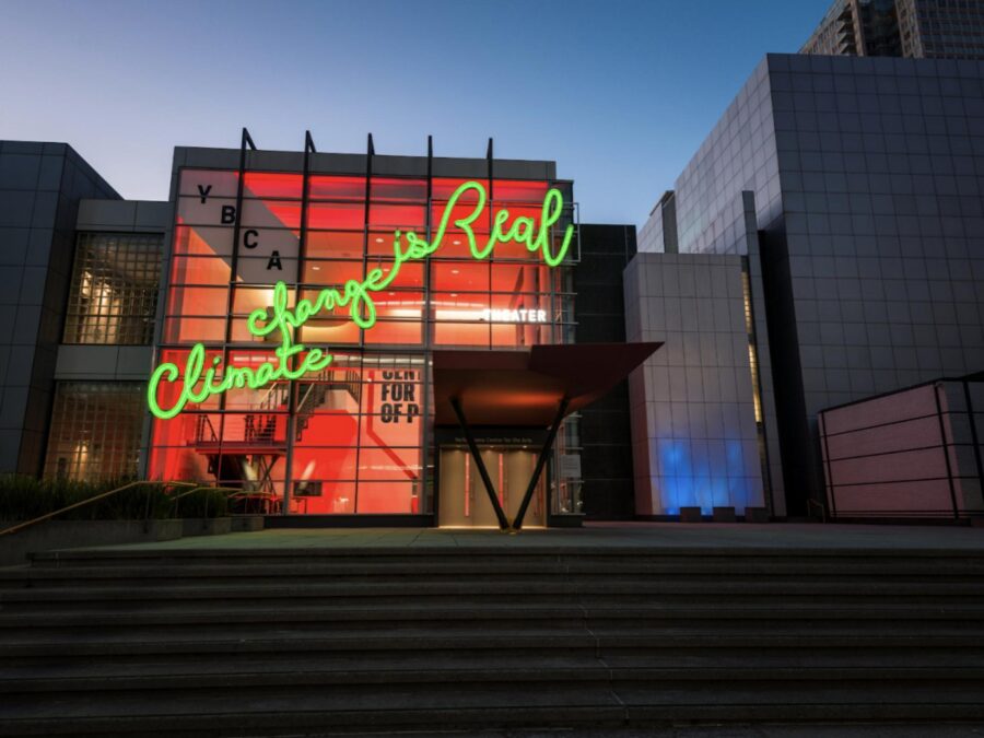 exterior of building with large neon green light formed into cursive text on the windows reading climate change is real