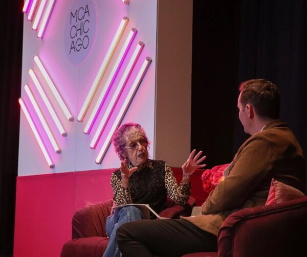 Two people sit on a red couch facing each other