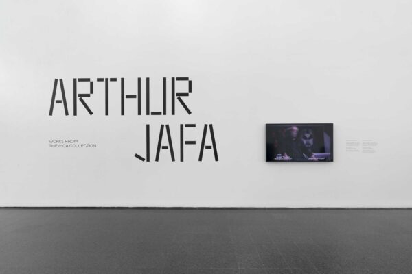 Large font reading Arthur Jafa on a white wall next to a small video screen