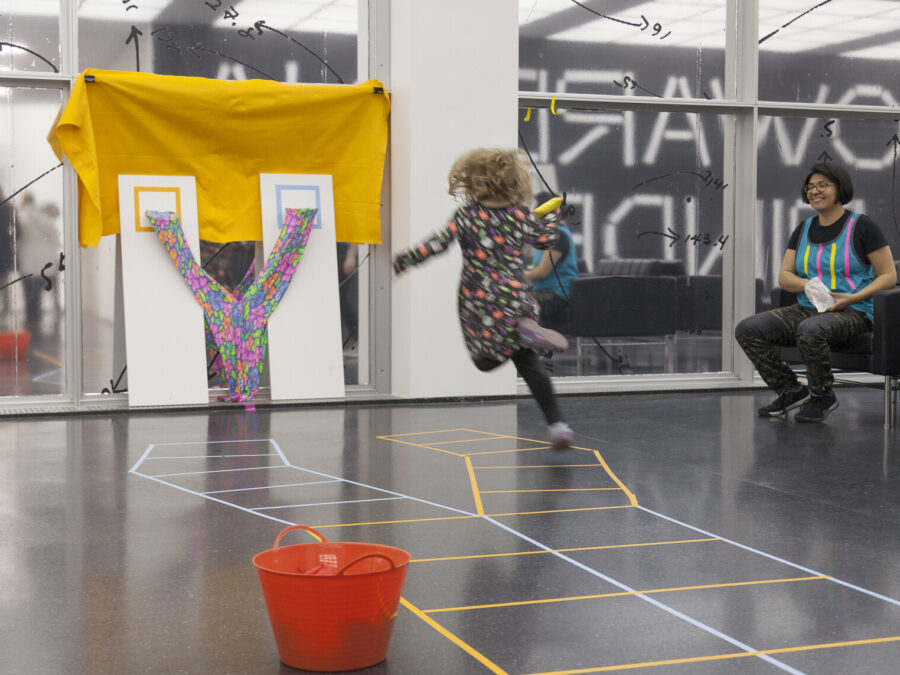 A child in midair aims a beanbag at a makeshift goal as an adult watches on.
