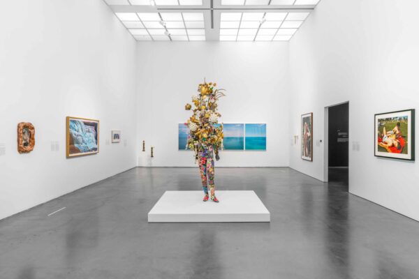 a sculpture of flowers in the shape of a human form on a pedestal in a room with artworks on the wall