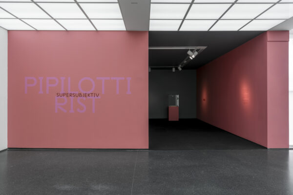A pink wall with large text reading Pipilotti Rist leads to a darkened room with three spot lit areas