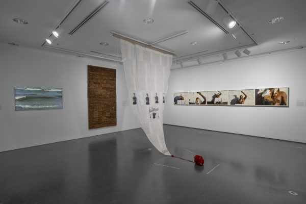 Gallery with several artworks hanging on the wall and a sail-like object hanging from the ceiling in the middle