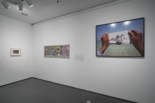 Corner of gallery wall with two artworks hanging on the right wall, one on the left.