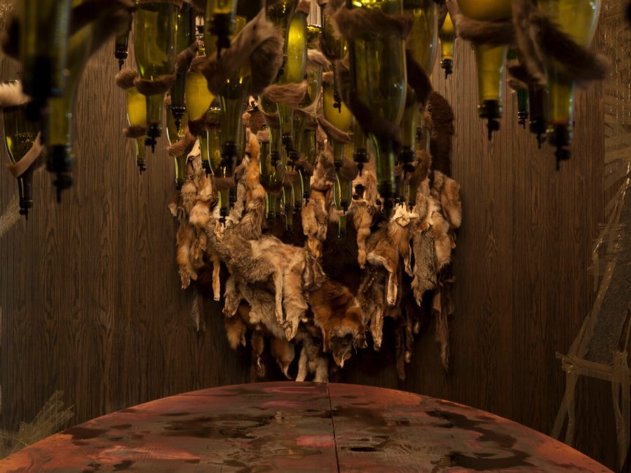 A wood-clad room filled with hanging animal pelts and corked wine bottles over a table.