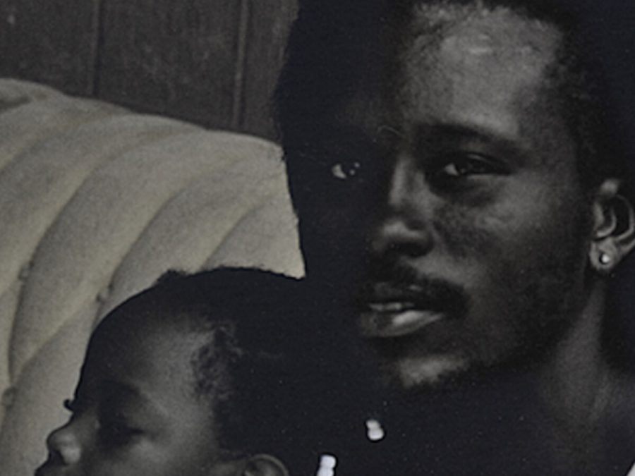 Black and white grainy image of a man with dark skin holding a small child on a couch