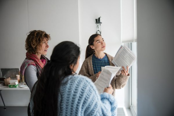 Three people standing in a semicircle look off into the distance. In their hands they hold a handful of paper.
