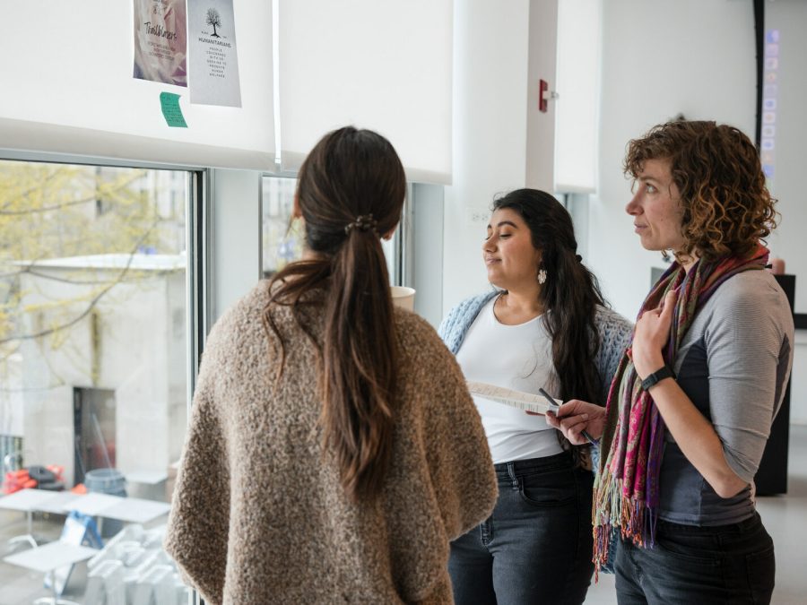 Three people gather around pieces of paper taped to a window shade in a bright white studio space