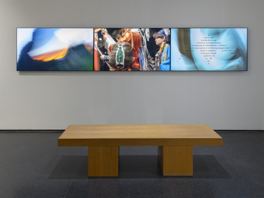 Three screens hang on a light gray wall in front of a chunky wooden bench.