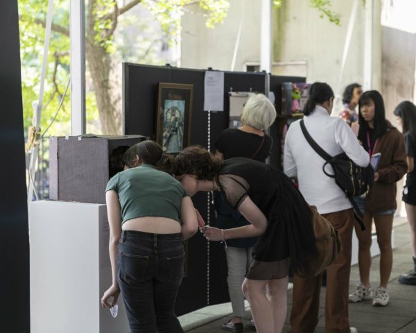 People gather around artworks hung on divider walls next to windows.